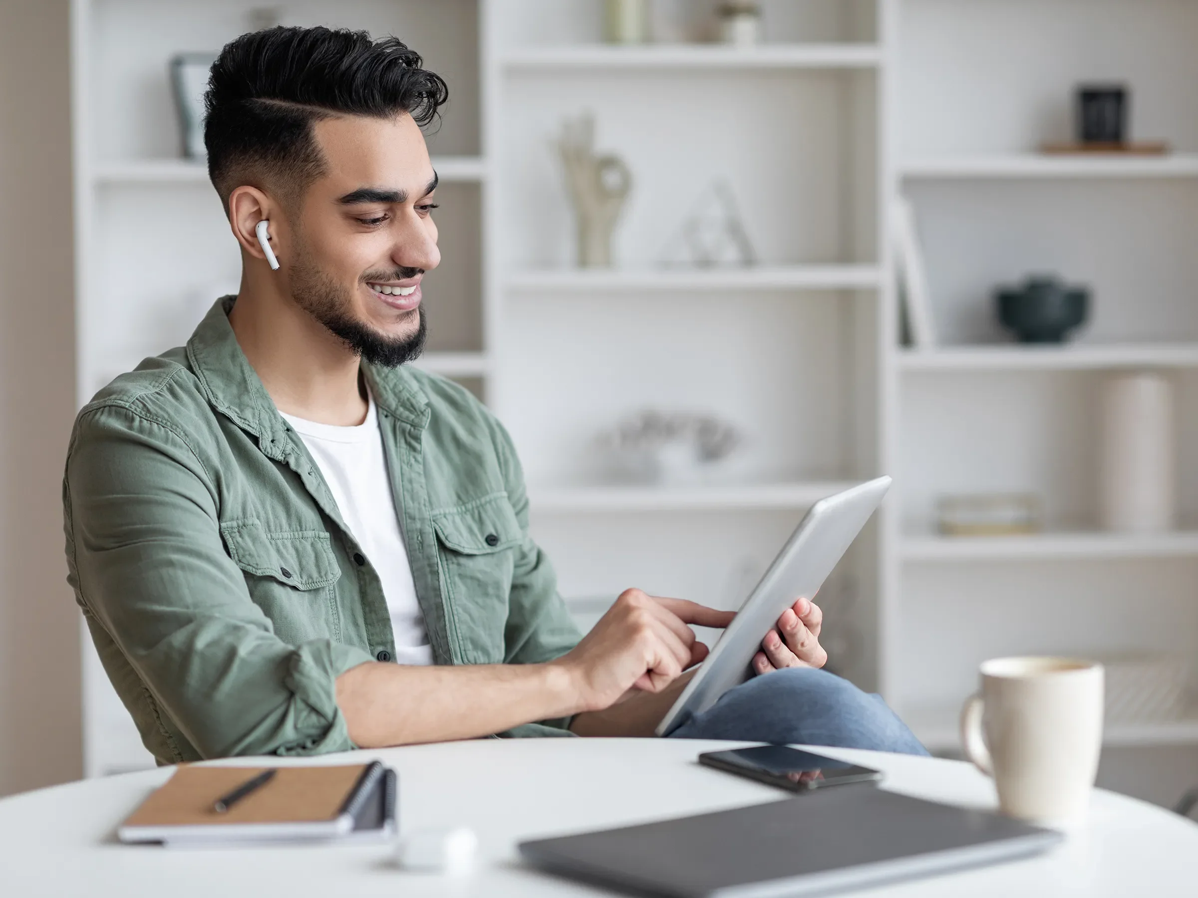 Man in front of a bookcase looking at a tablet and listening on earbuds